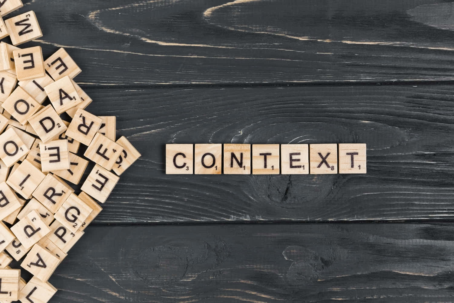 Gros plan sur des tuiles de Scrabble disposées sur fond de bois sombre, formant le mot « CONTEXT » au centre, avec d'autres tuiles éparpillées à gauche en tas désordonné.